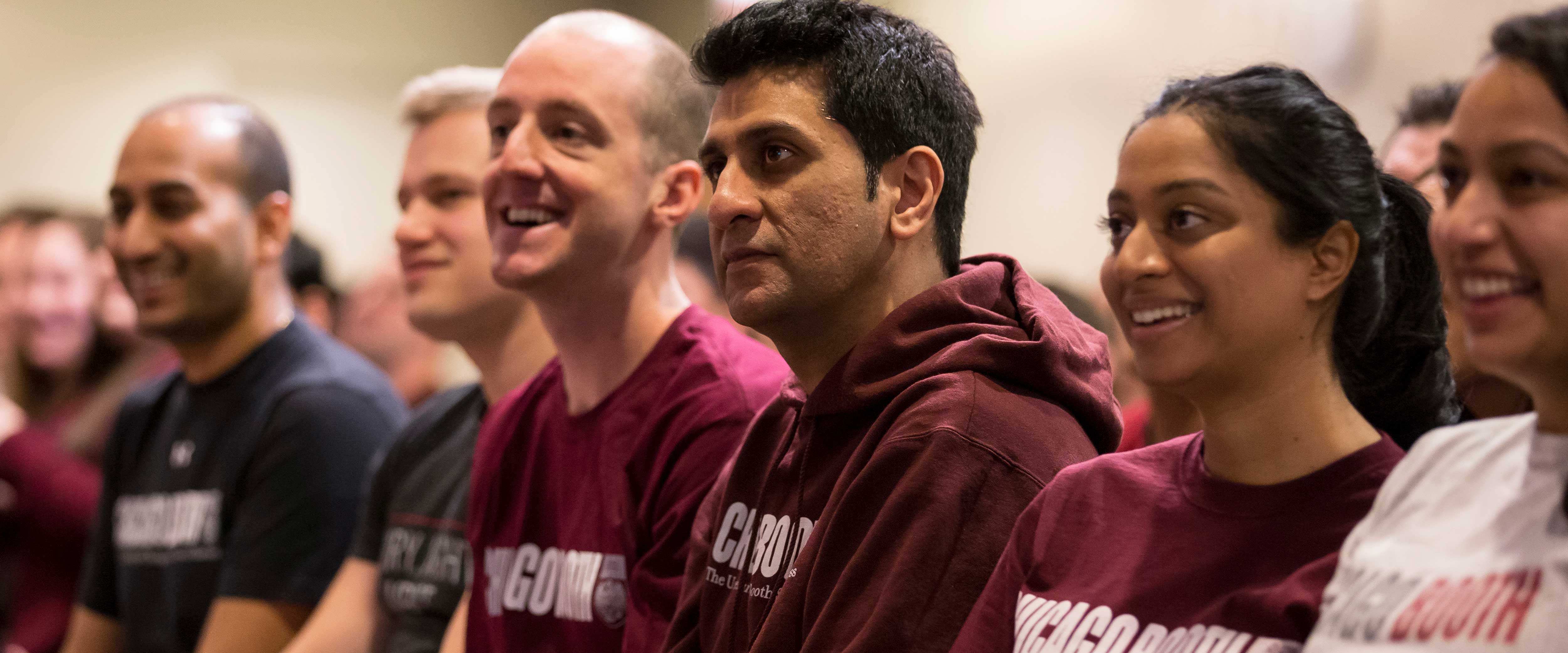 Group of students and alumni in Chicago Booth gear listening to a speaker at an event