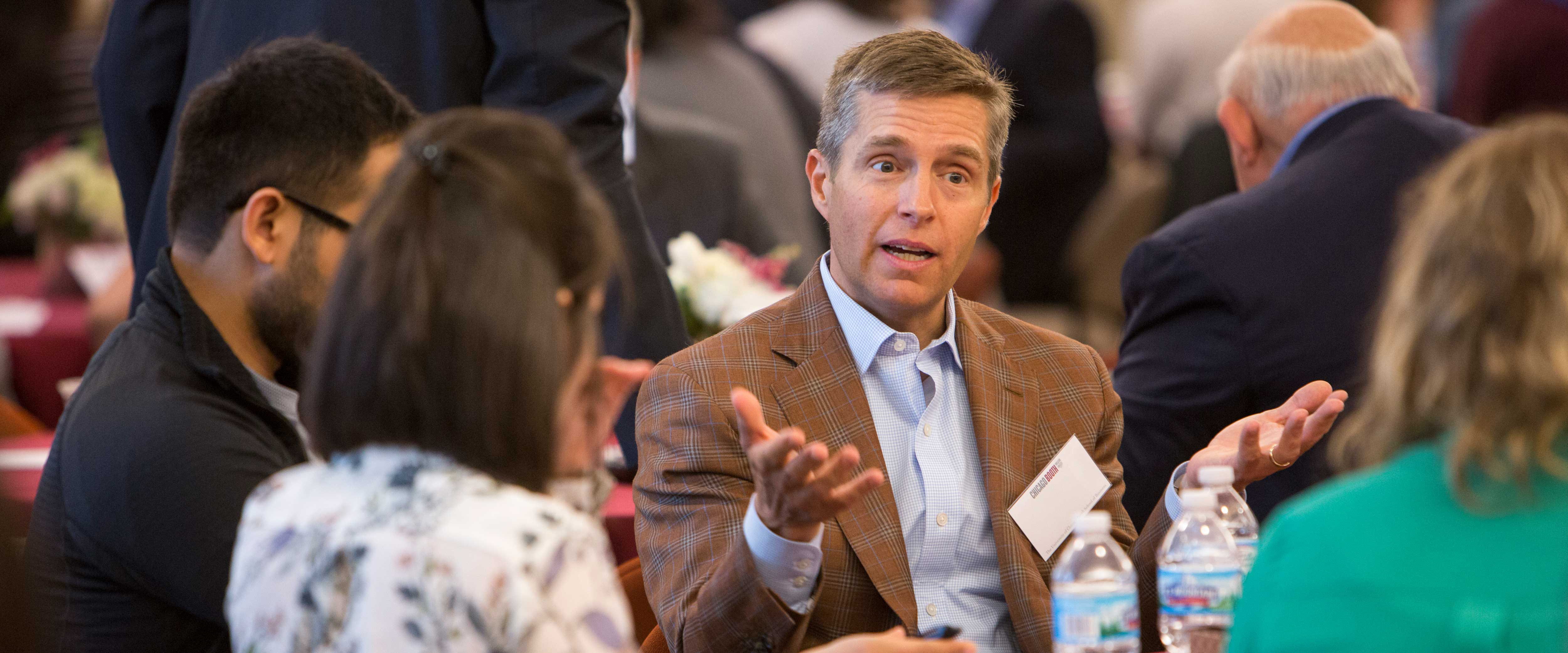 Booth alumnus speaking to a table of students